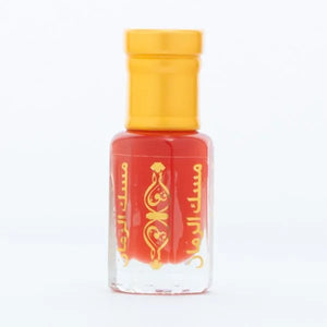 Gold-capped pomegranate perfume oil bottle labeled Musk Al Rumman sitting on snow with red fruit pieces – Arabic attar for men and women